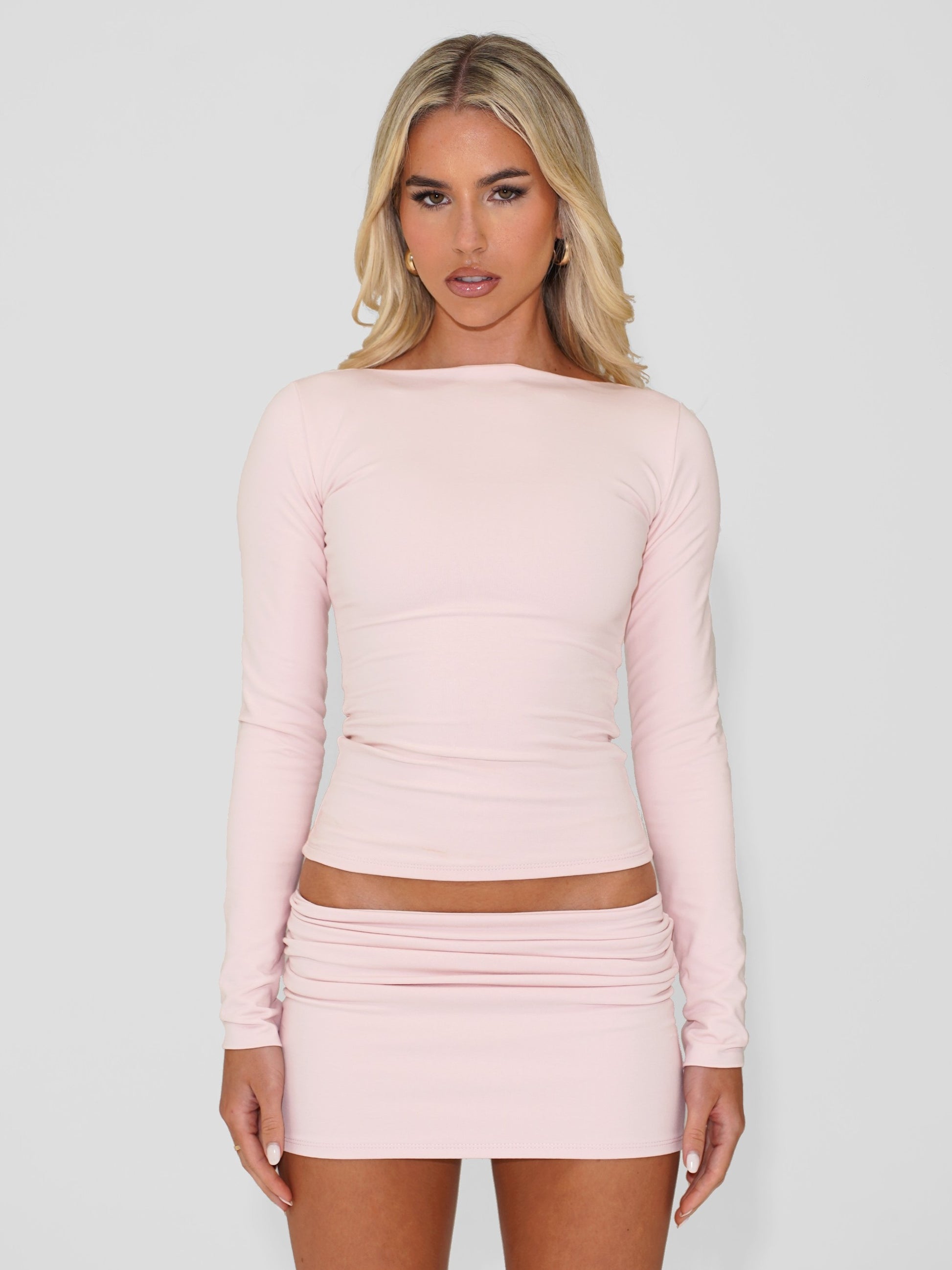 Model wearing light pink long sleeve cotton top and matching mini skirt, against white background.