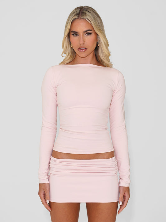 Model wearing light pink long sleeve cotton top and matching mini skirt, against white background.