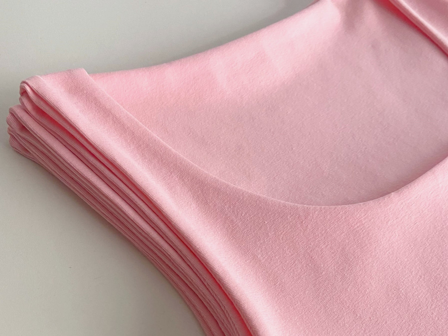 Close up of pink cotton double-layered vest tops neatly stacked on a white background.