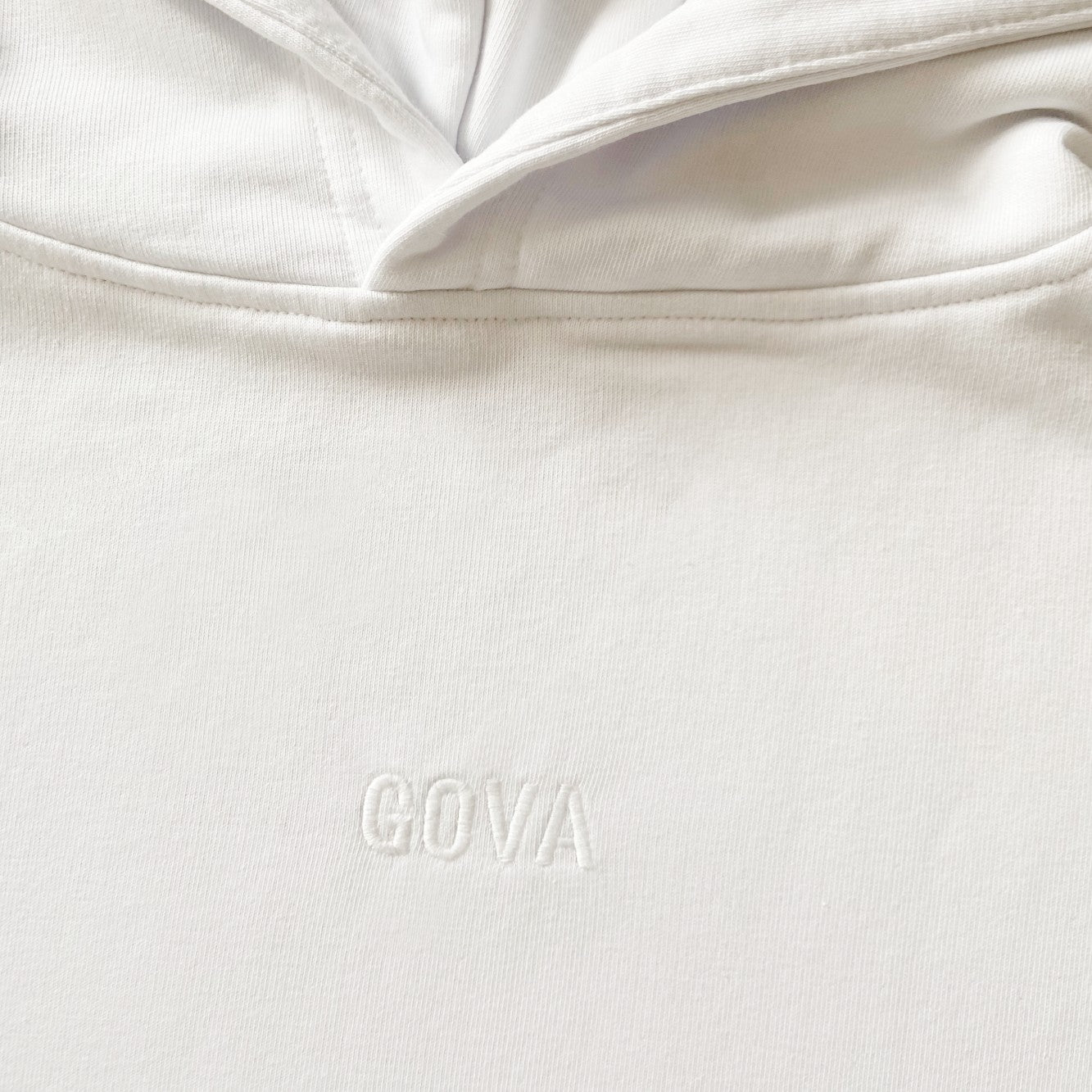 Close up of white embroidered logo detail on white cotton hoodie.