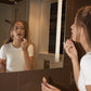 Girl applying lip gloss in front of a bathroom mirror.