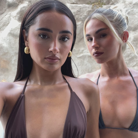 Girls in blue and brown tie bikinis in front of stone wall.